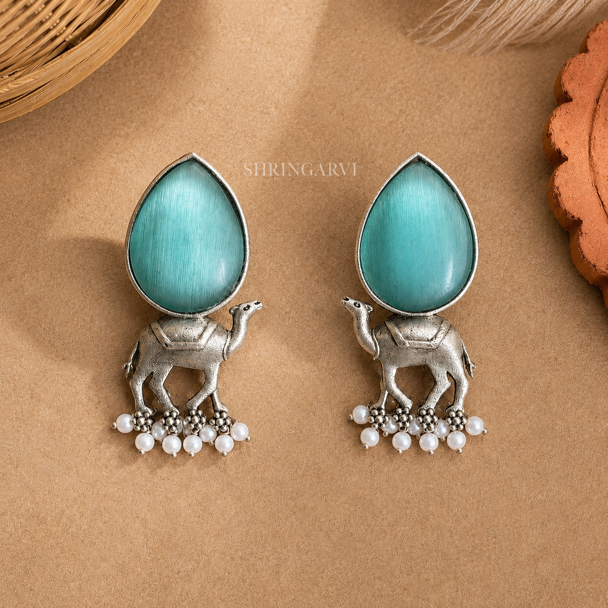 Handcrafted Aqua Blue Monalisa Camel Danglers in oxidised brass featuring teardrop Aqua Blue Monalisa stones, detailed camel motifs, and pearl drop accents for festive and ethnic styling.