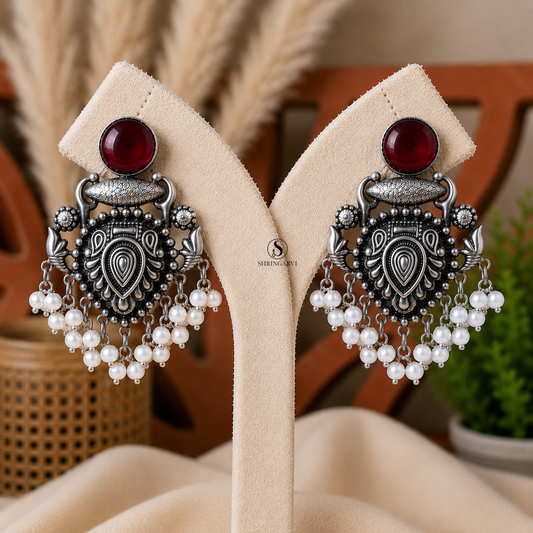 Handcrafted Deep Maroon Raagini Danglers in oxidised brass featuring a ruby red stone, intricate traditional motifs, and elegant pearl drop accents for festive and ethnic styling.