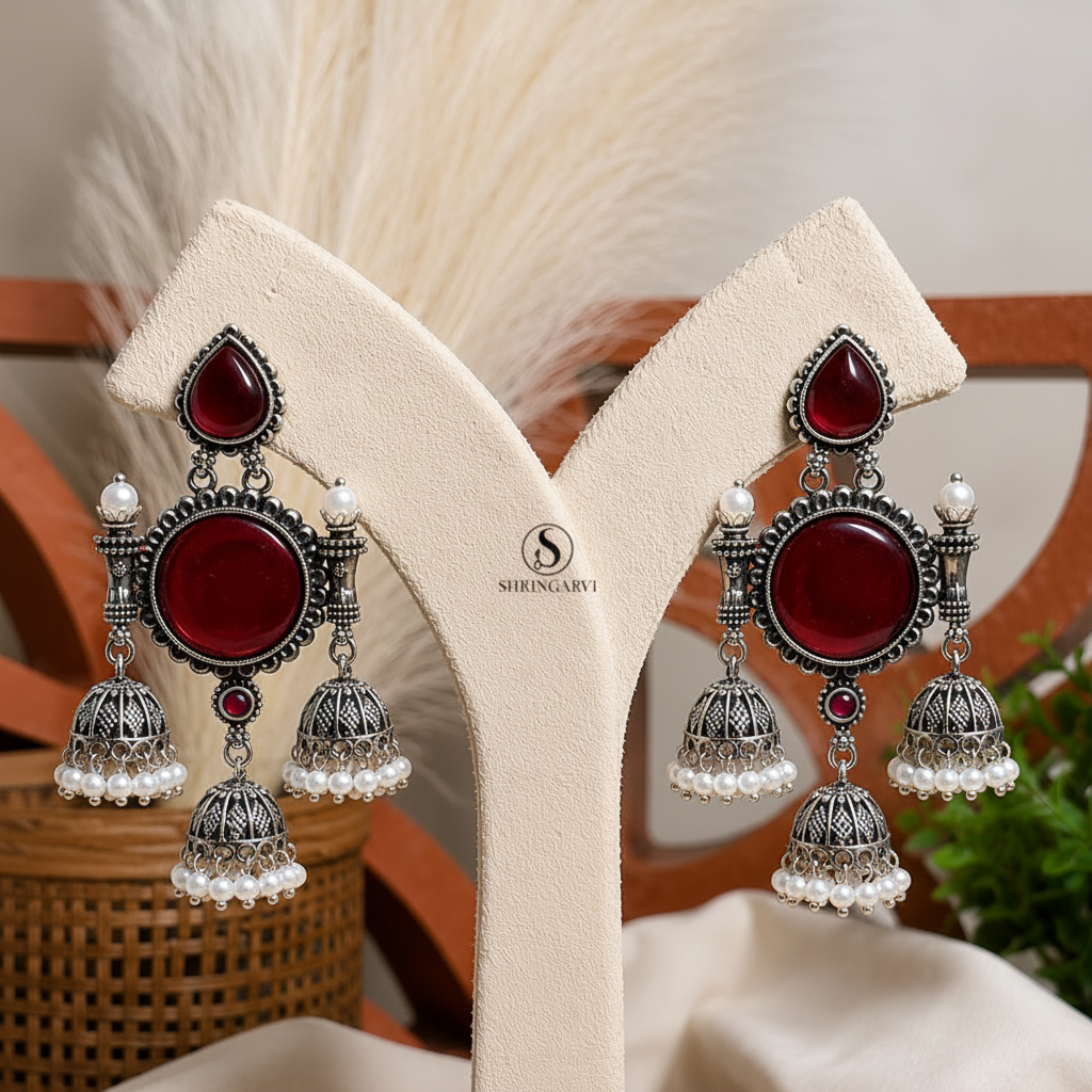 Handcrafted Deep Maroon Tripuri Jhumkas in oxidised brass featuring deep maroon stones, pearl-accented jhumkas, and intricate traditional detailing for festive and ethnic styling.