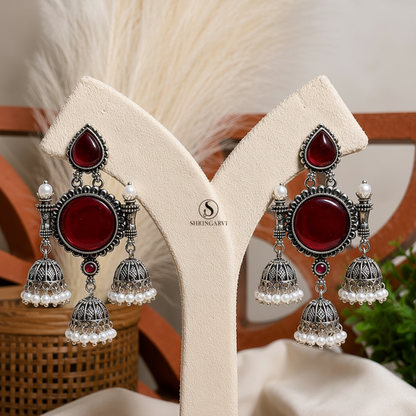 Handcrafted Deep Maroon Tripuri Jhumkas in oxidised brass featuring deep maroon stones, pearl-accented jhumkas, and intricate traditional detailing for festive and ethnic styling.
