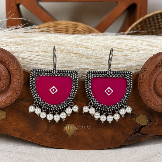 Handcrafted magenta  Bindu oxidised brass danglers featuring magenta Meenakari enamel detailing, intricate oxidised border, and pearl drop accents for festive and ethnic styling.