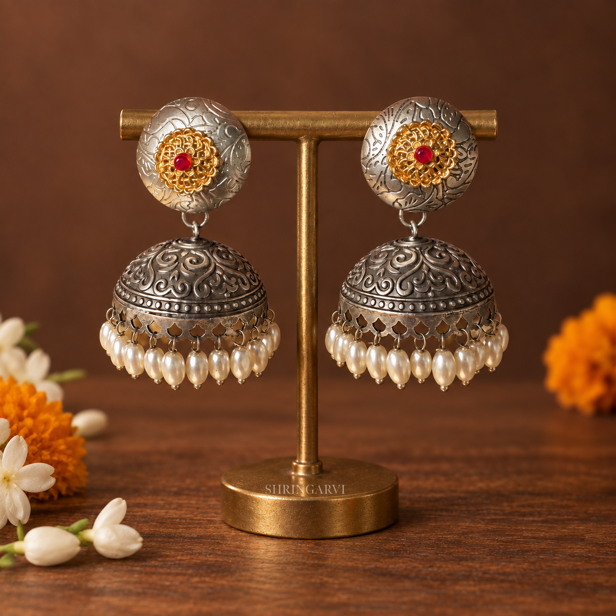 Radhya dual tone oxidised jhumka earrings with gold floral motif, red stone center, engraved silver finish, and pearl drop detailing.